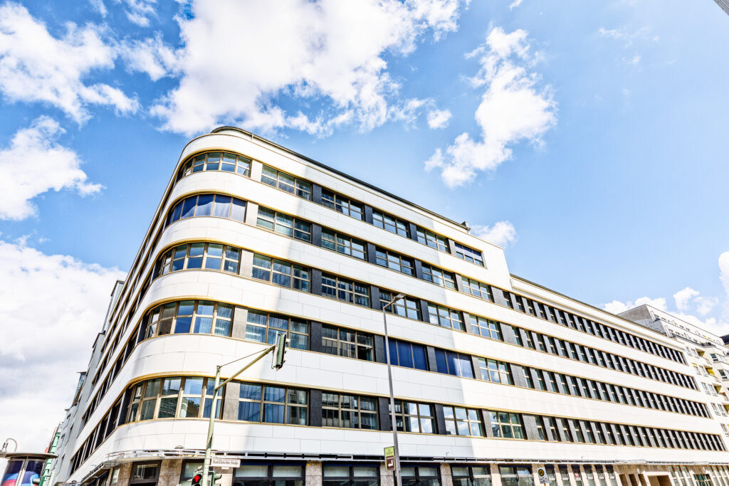 Moderne Architektur eines mehrstöckigen Gebäudes mit geschwungener Fassade und großen Fenstern vor einem blauen Himmel.