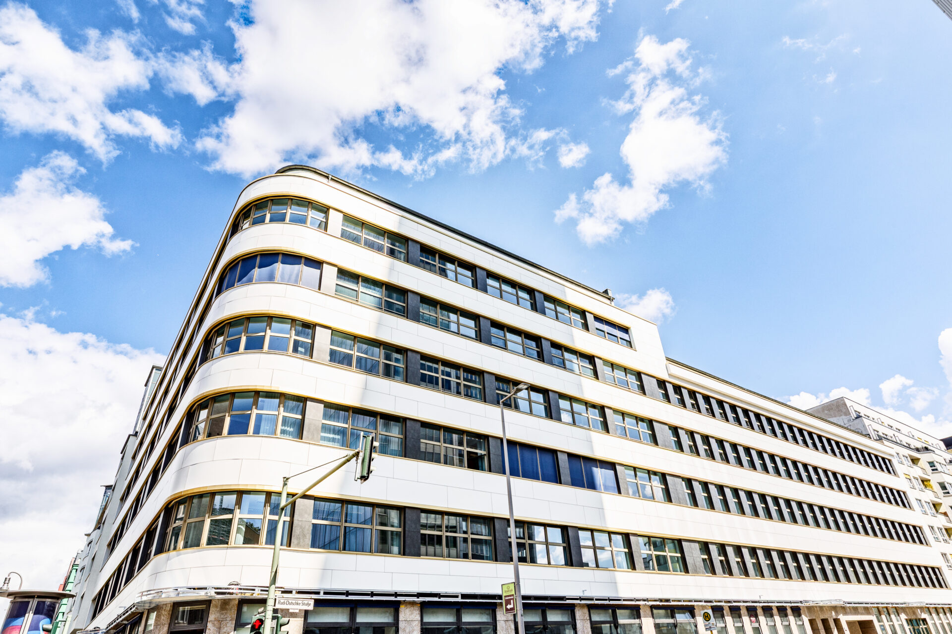 Moderne Architektur eines mehrstöckigen Gebäudes mit geschwungener Fassade und großen Fenstern vor einem blauen Himmel.