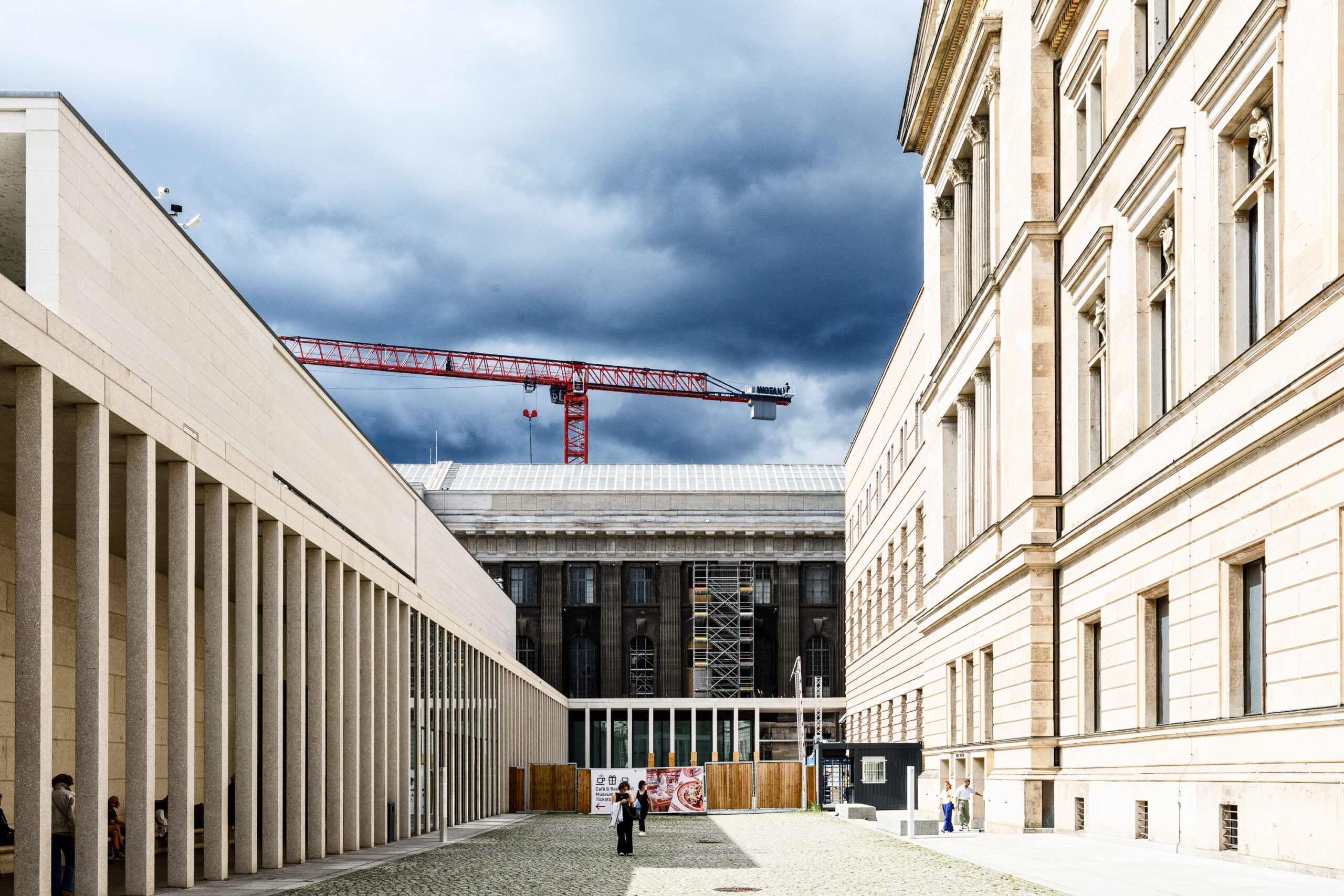 Blick auf einen Innenhof mit modernen und historischen Gebäuden, einem Baukran und Menschen, die sich im Raum bewegen.